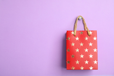 Photo of Red shopping paper bag with star pattern on violet background, space for text