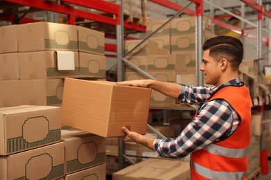 Photo of Worker stacking cardboard boxes in warehouse. Wholesaling