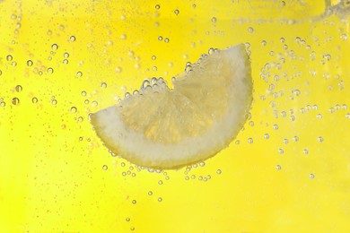Photo of Juicy lemon slice in soda water against yellow background, closeup