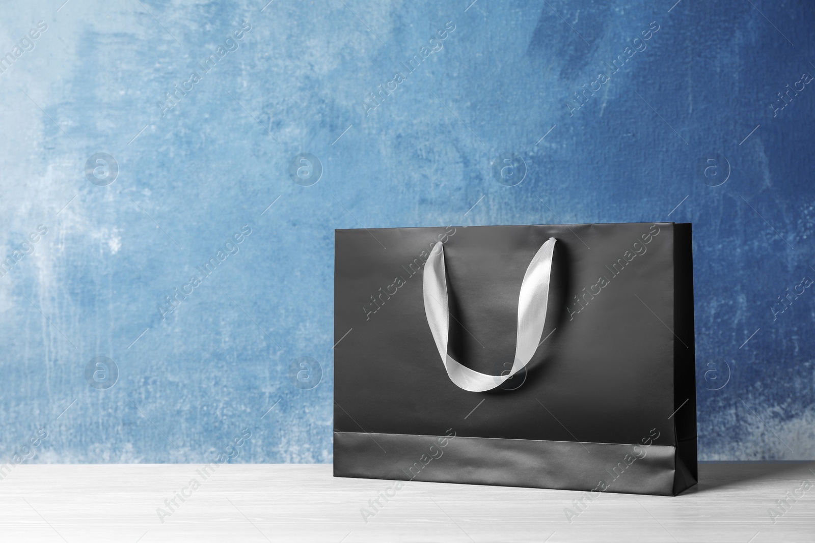 Photo of Paper shopping bag with handles on table against color wall. Mock up for design