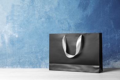 Paper shopping bag with handles on table against color wall. Mock up for design