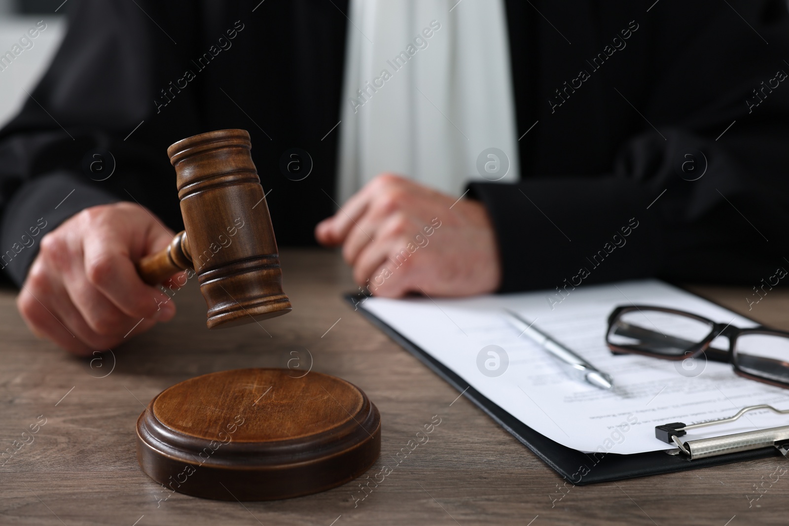 Photo of Judge with gavel and papers sitting at wooden table, closeup