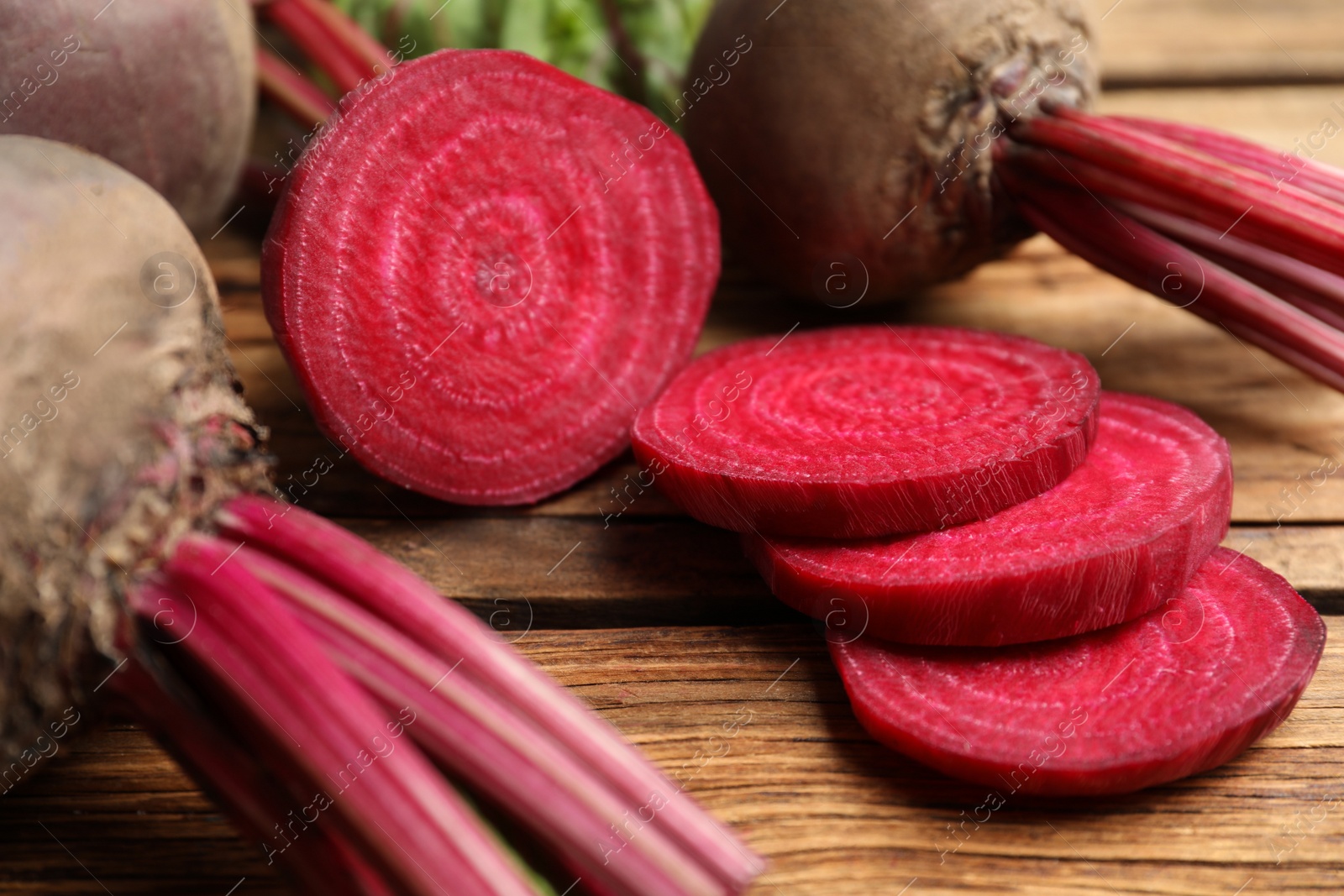 Photo of Cut and whole raw beets on wooden table, closeup