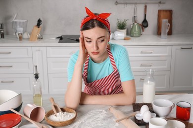 Photo of Upset housewife at messy countertop in kitchen. Many dirty dishware, food leftovers and utensils on table