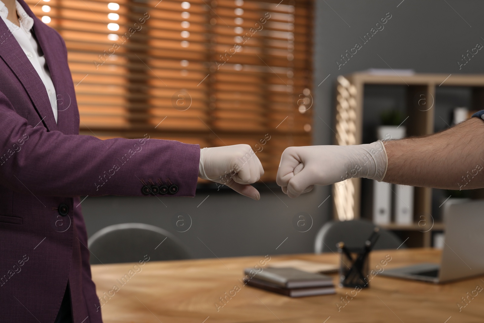 Photo of Office employees greeting each other by bumping fists at workplace, closeup