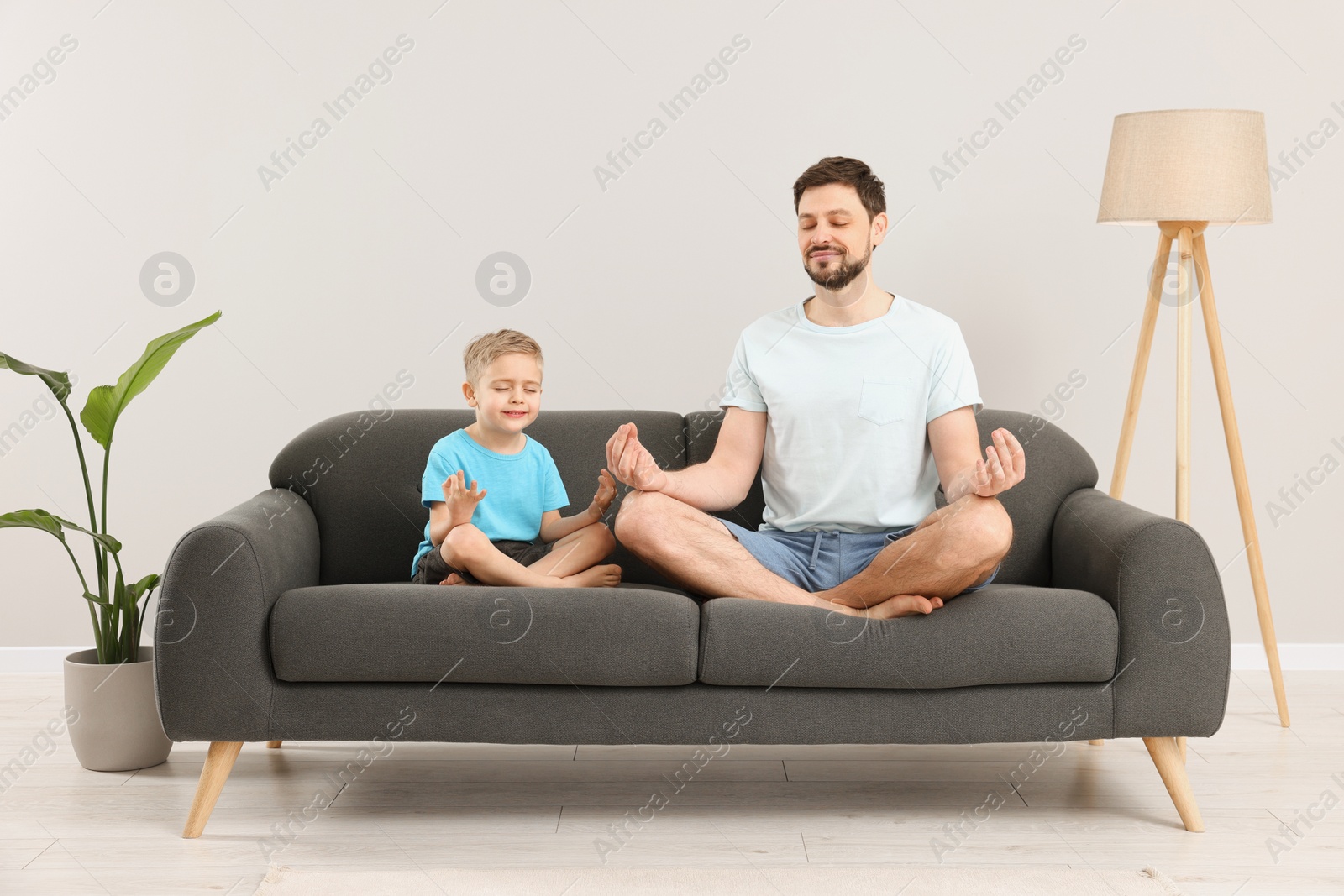 Photo of Father with son meditating together on sofa at home. Harmony and zen