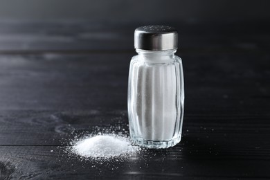 Photo of Organic salt in glass shaker on black wooden table, closeup