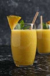 Photo of Tasty pineapple smoothie in glasses on black textured table