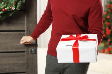 Photo of Young man in Santa hat with Christmas gift box received by mail indoors, closeup