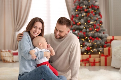 Happy family with cute baby in room decorated for Christmas holiday