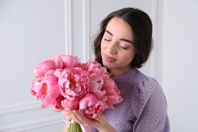 Beautiful young woman with bouquet of pink peonies near white wall