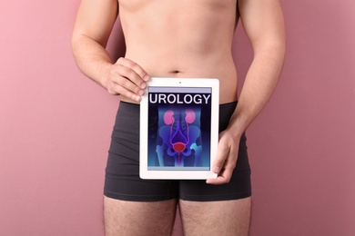Photo of Young man holding tablet with urinary system on screen against color background