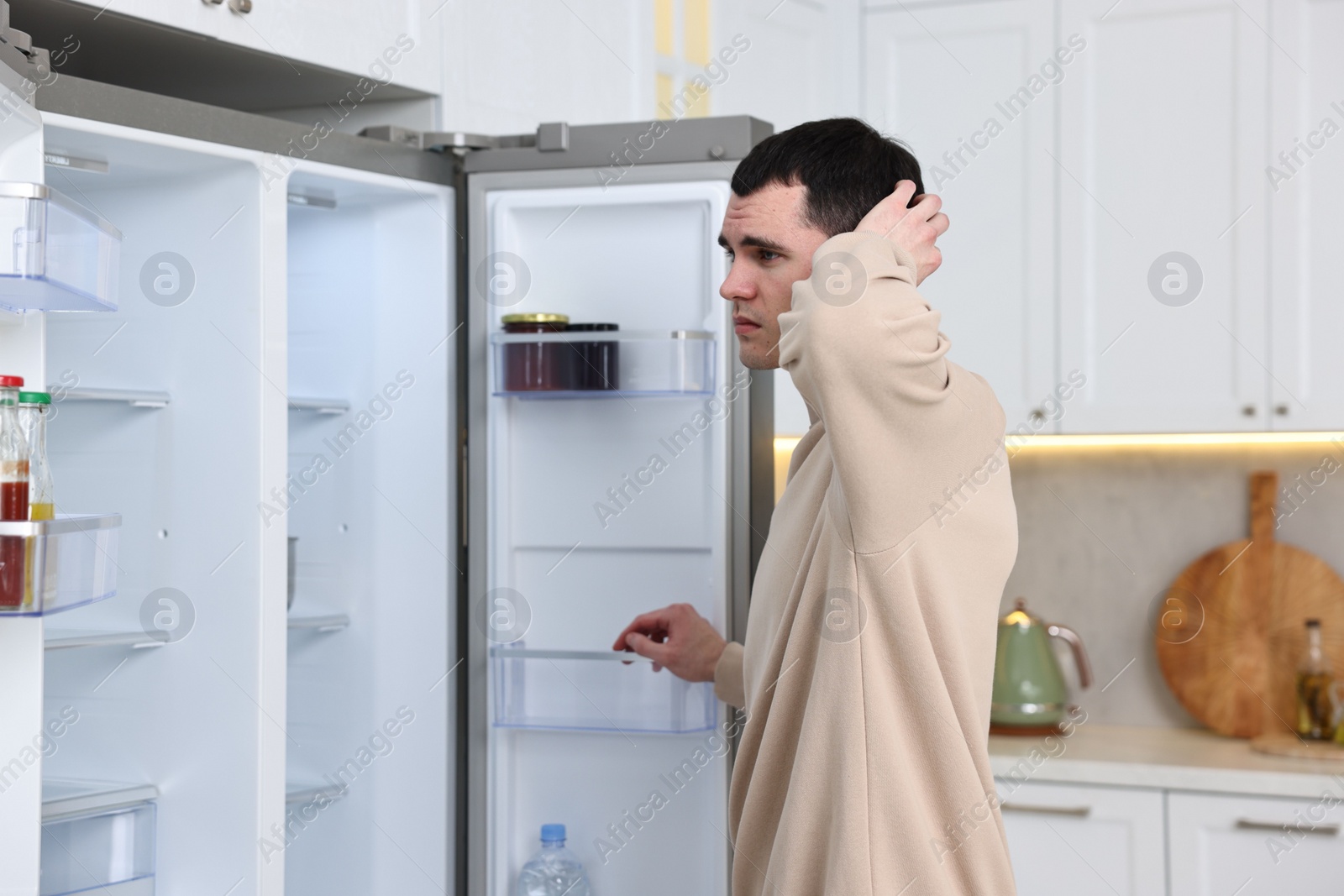 Photo of Thoughtful man near empty refrigerator in kitchen