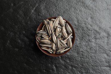 Photo of Raw sunflower seeds in bowl on black background, top view