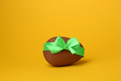 Photo of One tasty chocolate egg with green ribbon on orange background