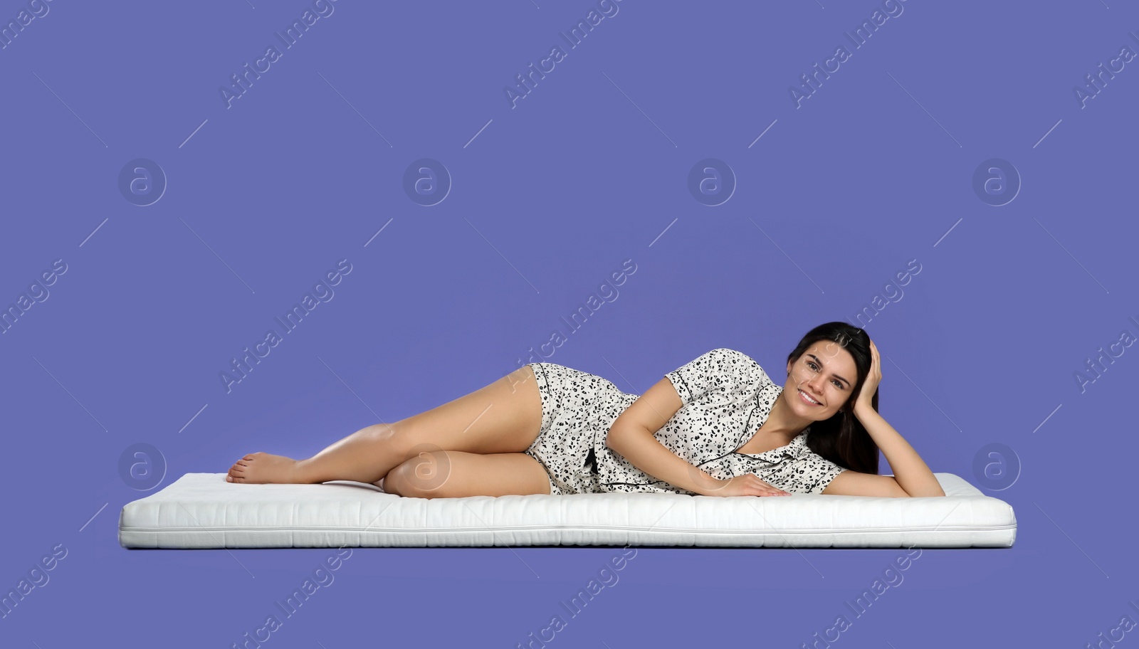 Photo of Young woman lying on soft mattress against light purple background