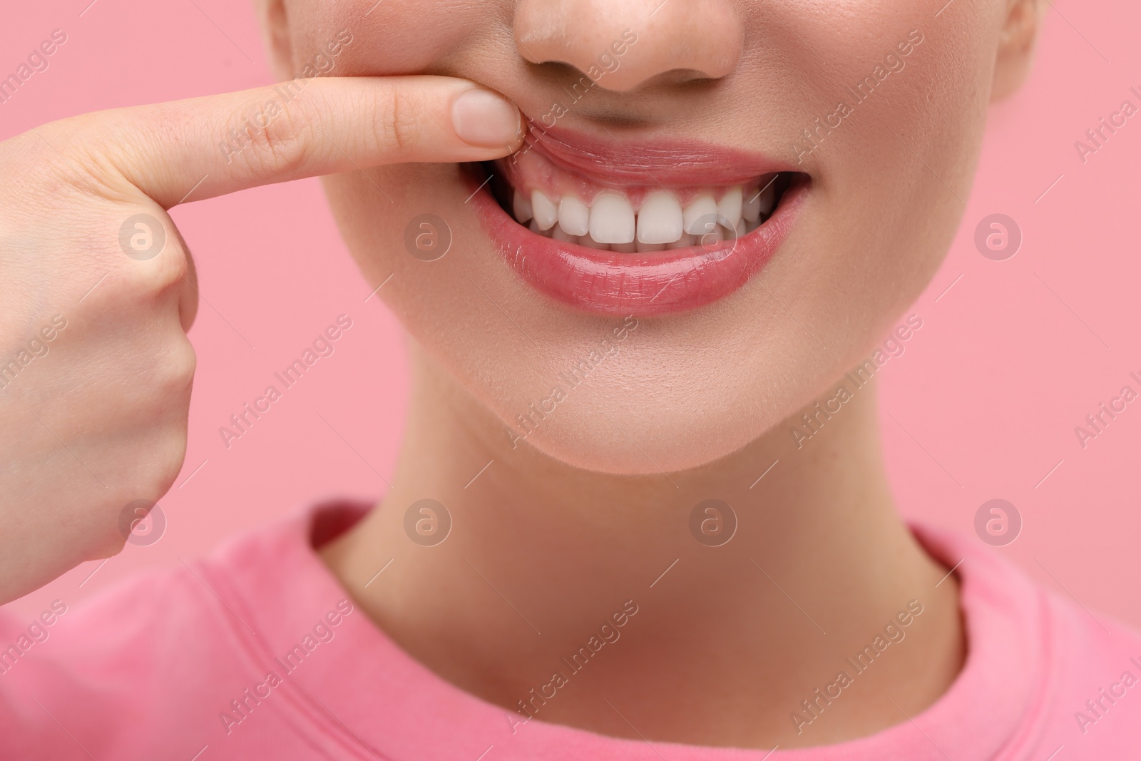 Photo of Beautiful woman showing her clean teeth on pink background, closeup