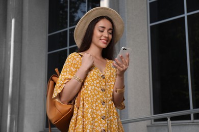 Beautiful young woman with stylish backpack and smartphone outdoors