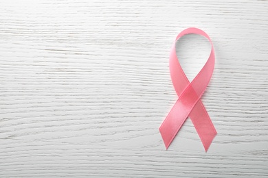 Photo of Pink ribbon on wooden background, top view with space for text. Breast cancer awareness concept