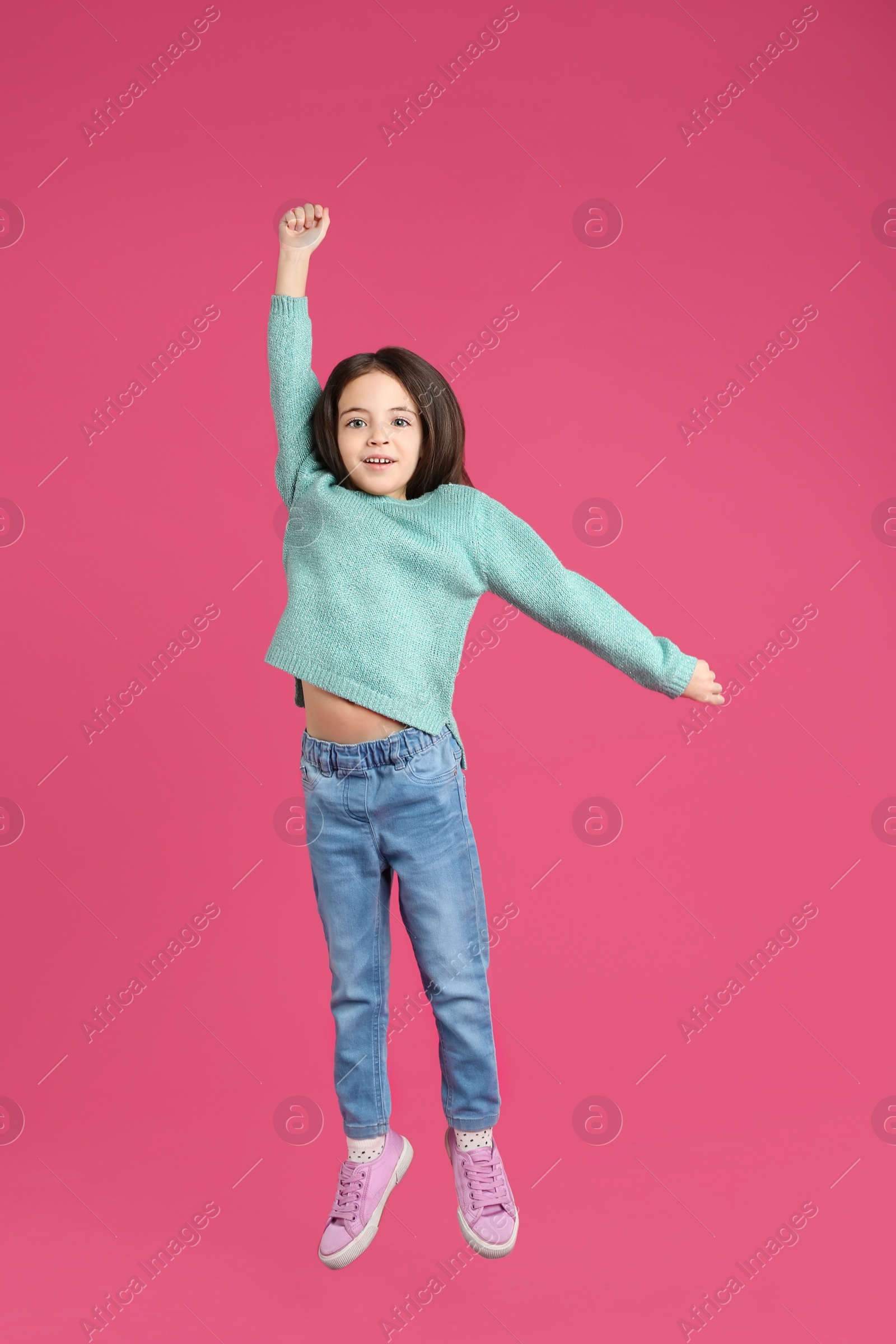 Photo of Cute little girl jumping on pink background