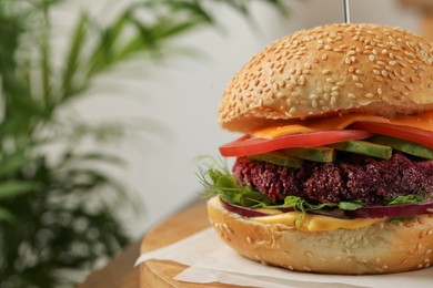 Photo of Tasty vegetarian burger with beet cutlet, cheese, avocado and tomato on wooden table, closeup. Space for text