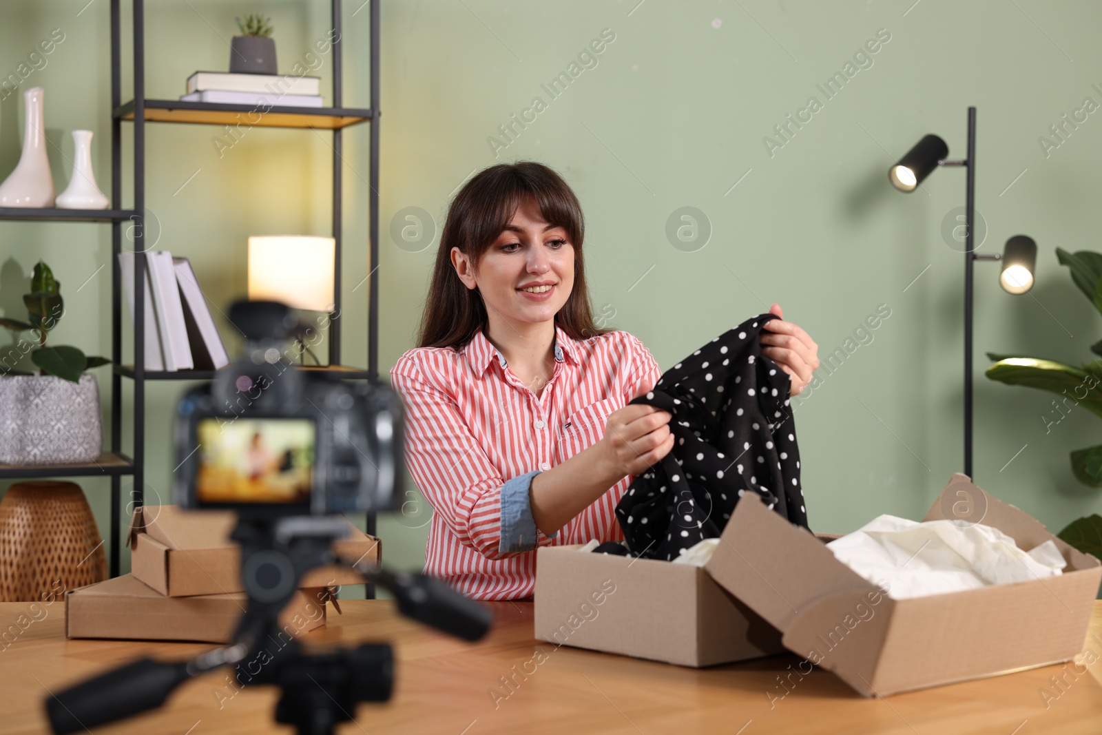 Photo of Smiling fashion blogger recording video while talking about clothes at home