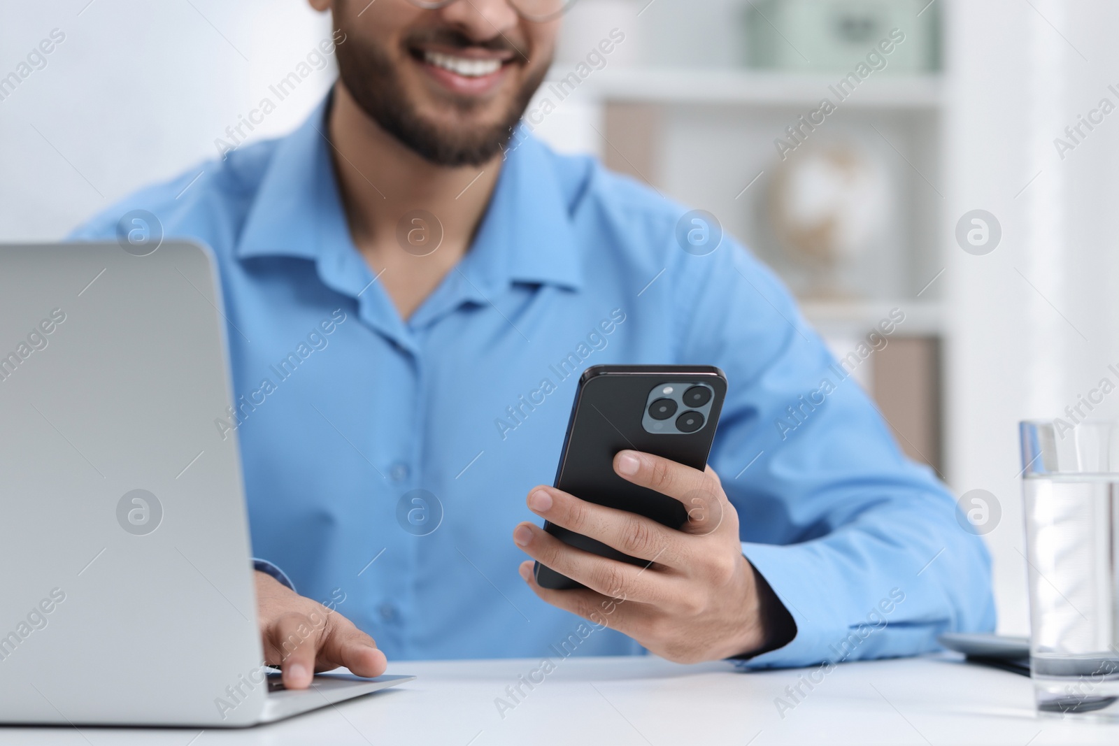 Photo of Man using smartphone while working with laptop at white table in office, closeup