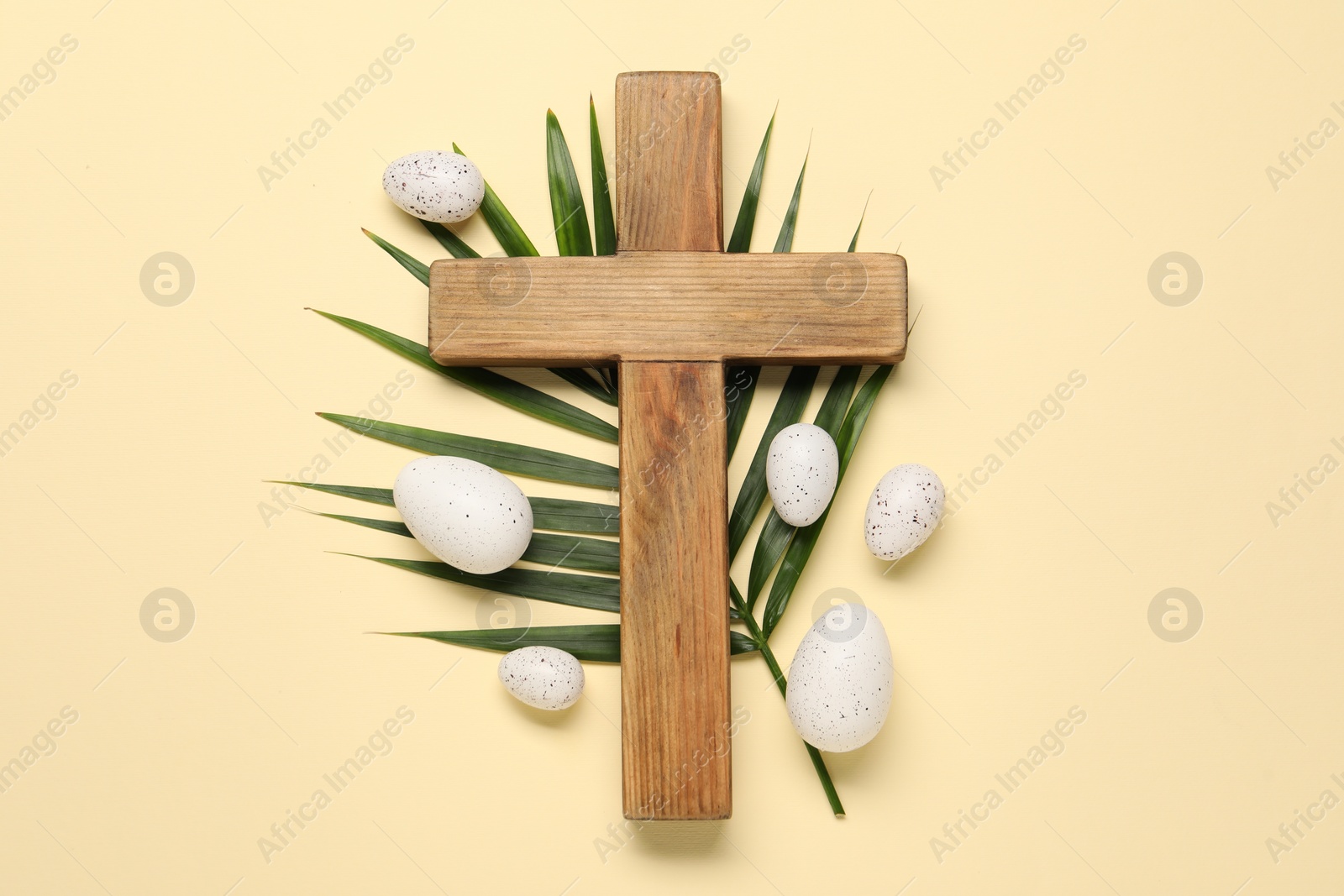 Photo of Wooden cross, painted Easter eggs and palm leaf on beige background, flat lay