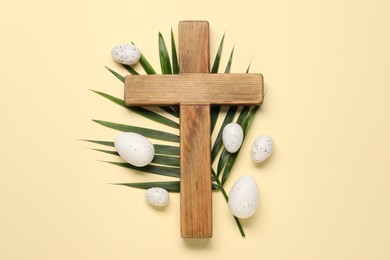 Wooden cross, painted Easter eggs and palm leaf on beige background, flat lay