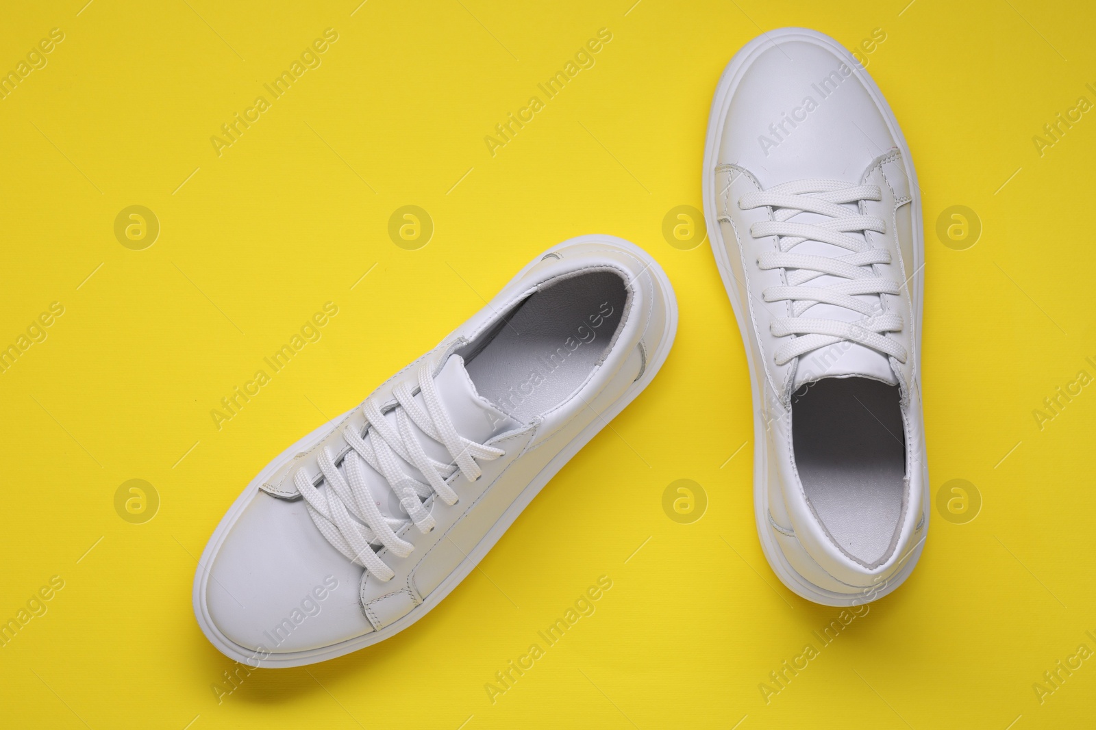 Photo of Pair of stylish white sneakers on yellow background, top view