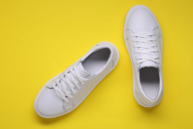 Pair of stylish white sneakers on yellow background, top view