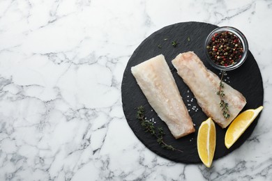 Photo of Fresh raw cod fillets, spices and lemon on white marble table, top view