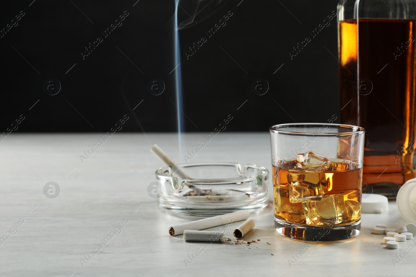 Photo of Alcohol and drug addiction. Whiskey in glass, bottle, cigarettes and pills on white table, space for text