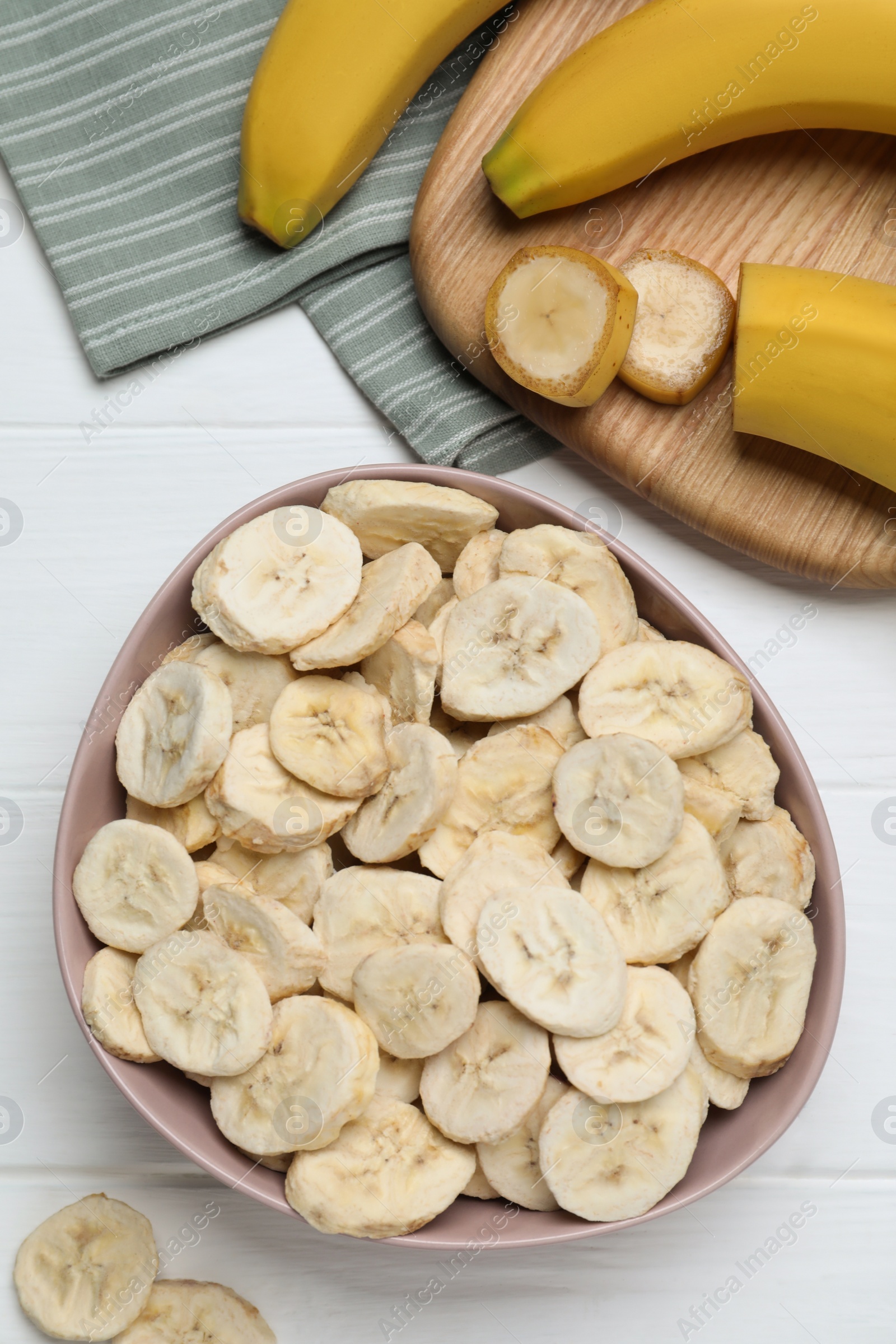 Photo of Freeze dried and fresh bananas on white wooden table, flat lay