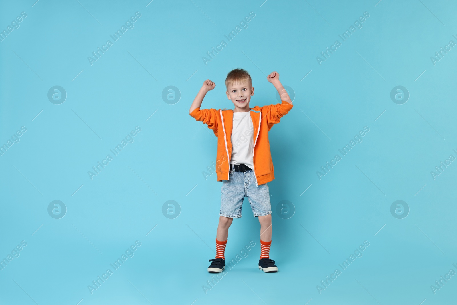 Photo of Happy little boy dancing on light blue background. Space for text