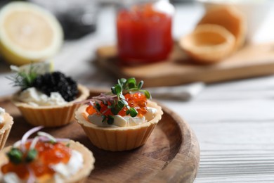 Photo of Delicious tartlets with red and black caviar served on white wooden table, closeup. Space for text