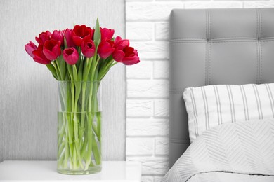 Photo of Bouquet of beautiful tulips in glass vase on white nightstand near bed