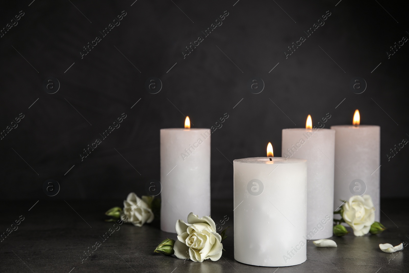 Photo of Burning candles and beautiful flowers on grey table, space for text