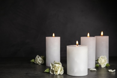 Burning candles and beautiful flowers on grey table, space for text