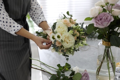 Photo of Florist making beautiful wedding bouquet at light grey table, closeup