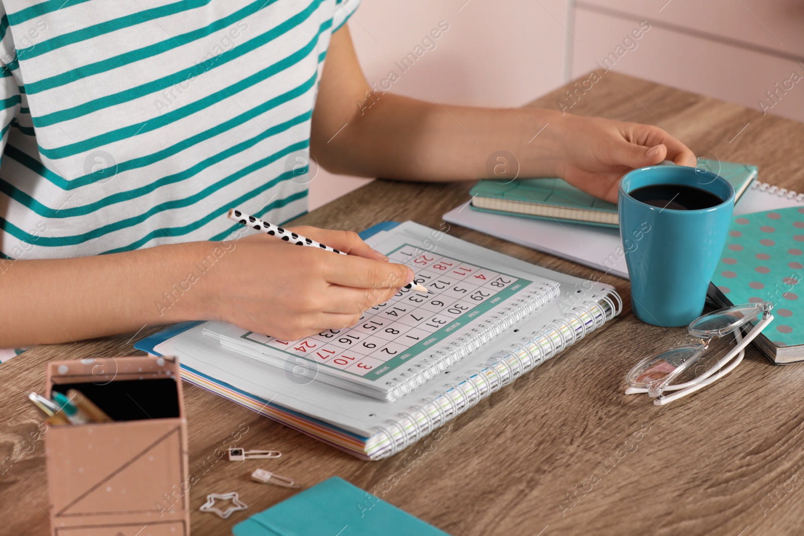 Photo of Woman marking date in calendar at wooden table, closeup