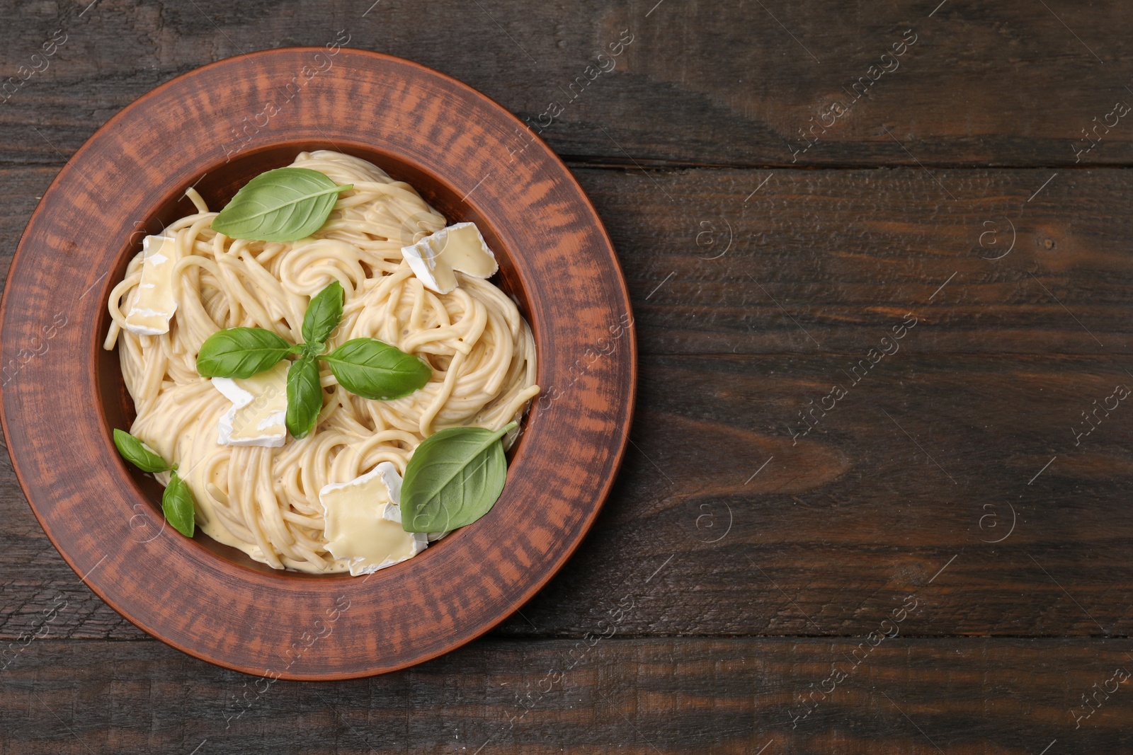Photo of Delicious pasta with brie cheese and basil leaves on wooden table, top view. Space for text