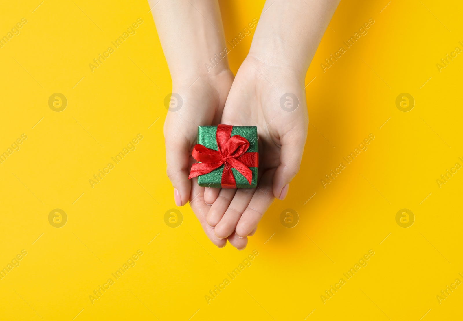 Photo of Christmas present. Woman holding beautifully wrapped gift box on yellow background, top view