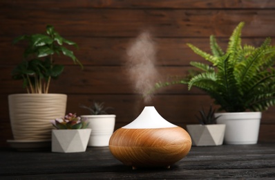 Photo of Composition with modern essential oil diffuser on black wooden table against brown background, space for text