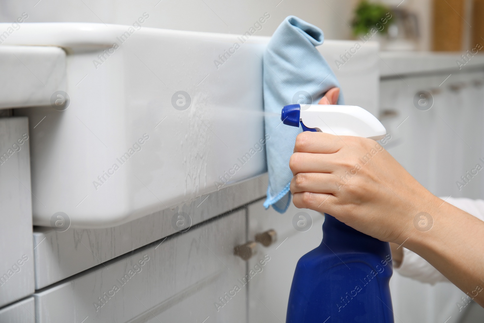 Photo of Woman cleaning white sink with rag and detergent in kitchen, closeup