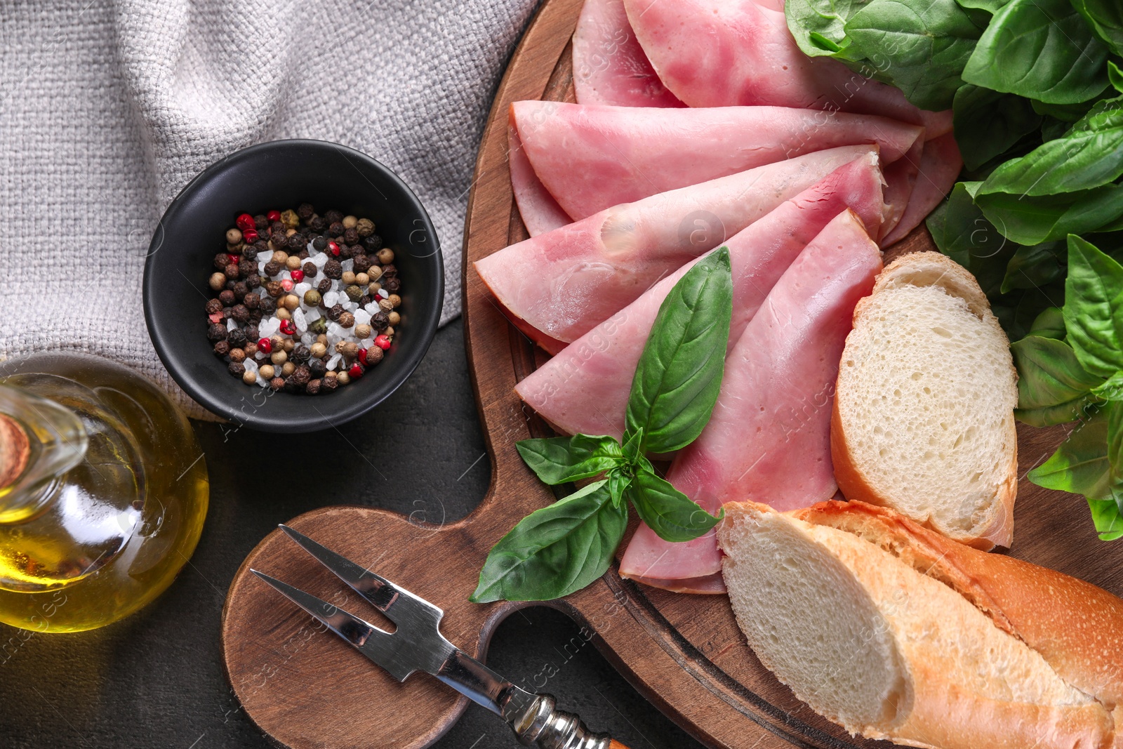 Photo of Tasty ham with basil, bread, spices and carving fork on table, flat lay