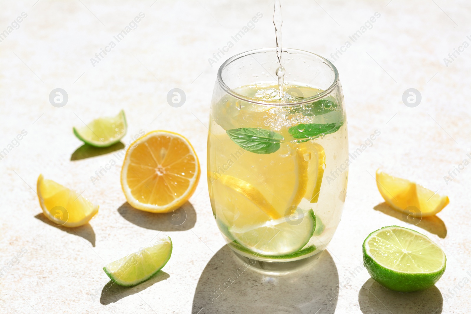 Photo of Pouring water into glass with lemon slices and mint at light grey table