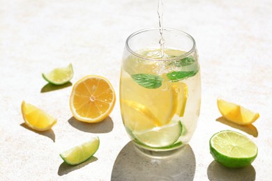 Photo of Pouring water into glass with lemon slices and mint at light grey table