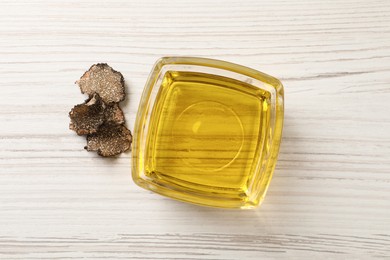 Fresh truffle oil in glass bowl on white wooden table, flat lay