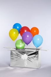 Photo of Gift box with bright air balloons on light background